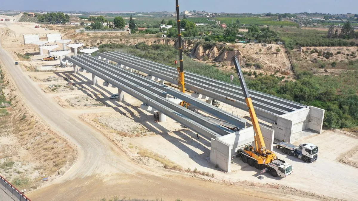 Vista aérea de un viaducto en construcción, con dos grúas colocando las vigas